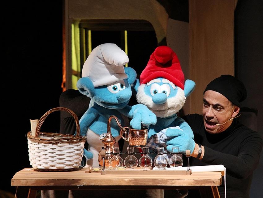Man sieht zwei Puppen – einen Schlumpf mit Papa Schlumpf und einen Schauspieler schwarz gekleidet.